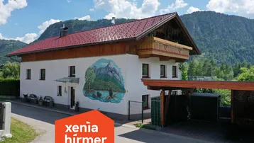 Traditionelles Haus mit Bergblick und Carport, umgeben von grüner Natur.