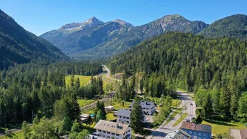 Malerisches Tal mit Straße, Fluss, Häusern und majestätischen Bergen unter blauem Himmel.