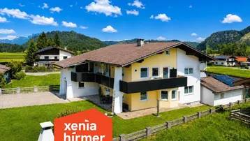 Großzügiges Einfamilienhaus mit gepflegtem Garten und Bergblick unter blauem Himmel.