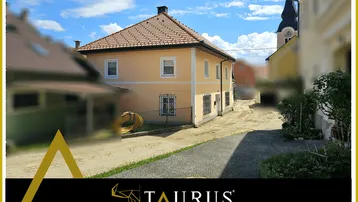 Traditionelles Wohnhaus mit Ziegeldach und Blick auf die Dorfkirche unter blauem Himmel.