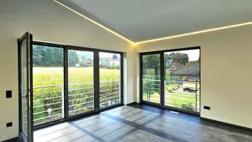 Heller Raum mit großen bodentiefen Fenstern und französischem Balkon, der einen weiten Blick ins Grüne bietet.