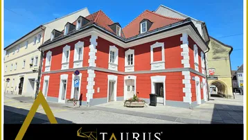 Historisches Gebäude mit markanter roter Fassade und weißen Akzenten an einer sonnigen Straßenecke.