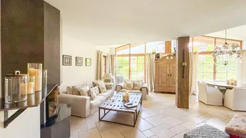 Geräumiger Wohn- und Essbereich mit Kamin, großen Fenstern und hellem Fliesenboden.
