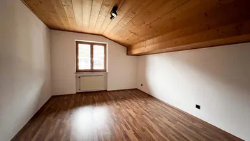 Schlafzimmer mit Holzdielenboden, Holzdecke und Fenster mit Blick ins Grüne.