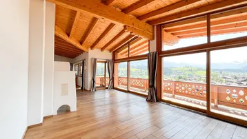 Geräumiges Wohnzimmer mit Holzbalkendecke, großen Fenstern und Zugang zum Balkon mit Bergblick.