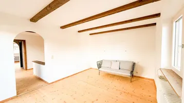 Helles Wohnzimmer mit sichtbaren Holzbalken an der Decke und hellem Holzfußboden.