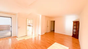 Helles Wohnzimmer mit Parkettboden, weißen Wänden und Zugang zu einem sonnigen Außenbereich.