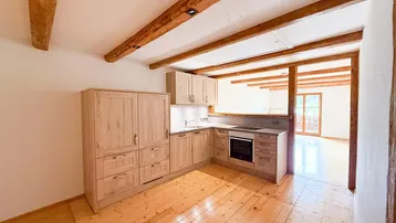 Moderne Holzküche mit Einbaugeräten, Holzbalken und Blick in den Wohnbereich.
