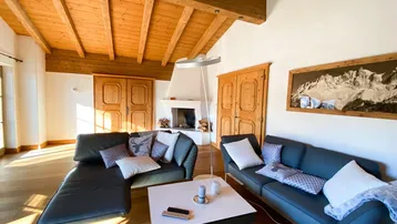 Gemütliches Wohnzimmer mit Holzbalkendecke, Kamin und bequemen Sofas, durchflutet von natürlichem Licht.