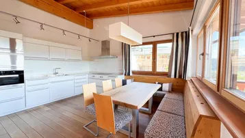 Moderne Einbauküche mit weißen Fronten, Essbereich und Holzbalkendecke in alpenländischem Stil.