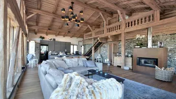 Geräumiger offener Wohnbereich mit Holzbalken, Kamin und integrierter Küche in einem Chalet-Stil.