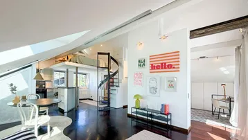 Helles und offenes Dachgeschoss-Wohnzimmer mit dunklem Holzboden, moderner Einrichtung und Zugang zu einer Schlafgalerie.