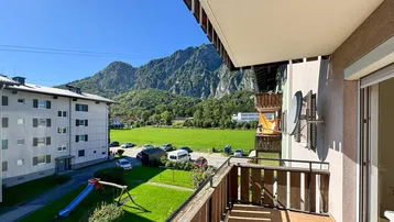 Sonniger Balkon mit Bergblick und Blick auf einen Spielplatz.