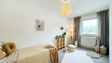 Freundliches Kinderzimmer mit Teppichboden, Einzelbett und Blick ins Grüne.