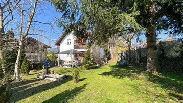 Sonniger Gartenbereich mit Rasenfläche, Bäumen und Blick auf das Wohnhaus.