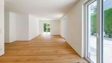 Helles, leeres Wohnzimmer mit Holzboden und Zugang zu einer Terrasse oder Garten.