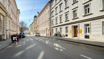 Blick auf eine belebte Straße mit historischen Gebäuden und geparkten Autos unter blauem Himmel.