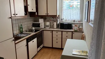 Funktionale Küche mit weißen Schränken, Essbereich und Holzfußboden, ausgestattet mit grundlegenden Geräten.