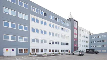 Modernes Geschäftsgebäude mit grauer und weißer Fassade, vielen Fenstern und einem Parkplatz davor.