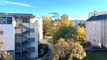 Blick auf eine Wohnsiedlung mit mehreren Gebäuden und herbstlichen Bäumen unter blauem Himmel.