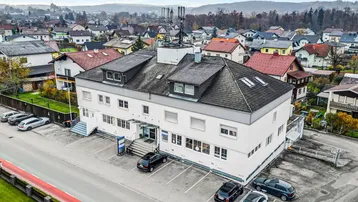 Luftaufnahme eines Mehrfamilienhauses mit Parkplätzen und umliegender Wohnbebauung in ländlicher Umgebung.