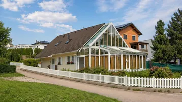 Charmantes Einfamilienhaus mit großem Wintergarten und weißem Lattenzaun in ländlicher Umgebung.