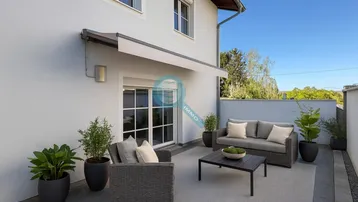 Moderne Terrasse mit bequemen Outdoor-Möbeln, Markise und Blick ins Grüne unter blauem Himmel.