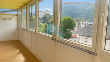 Heller Wintergarten mit großen Fenstern, Holzboden und weitem Blick auf die Berge und eine Burg.