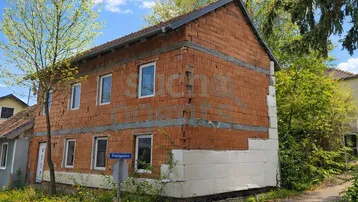 Rohbau eines Einfamilienhauses mit Ziegelmauerwerk und beginnender Dämmung an einer Straßenecke unter blauem Himmel.
