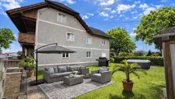 Sonniger Gartenbereich mit gemütlicher Lounge-Ecke, Grill und Whirlpool vor dem traditionellen Haus.