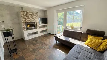 Gemütliches Wohnzimmer mit Kamin, bequemer Couch und großem Fenster mit Blick in die Natur.