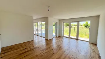 Helles Wohnzimmer mit Holzboden und großen Fenstern, die viel Tageslicht hereinlassen.