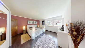 Gemütliches Schlafzimmer mit großem Bett, Holzboden und Blick ins Grüne durch das breite Fenster.