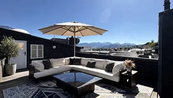 Großzügige Dachterrasse mit bequemen Loungemöbeln, Sonnenschirm und malerischem Bergblick.