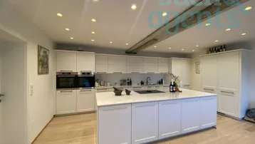 Moderne Küche mit weißer Einbauküche, großer Kochinsel und hellem Holzboden.