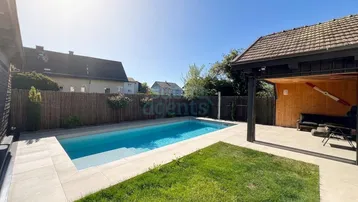 Sonniger Gartenbereich mit modernem Pool und angrenzendem Lounge-Bereich unter einem Holzpavillon.
