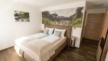 Gemütliches Schlafzimmer mit Doppelbett, Holzboden und einer dekorativen Wandtapete mit Landschaftsmotiv.