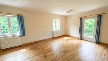 Helles Zimmer mit Holzboden, weißen Wänden und Zugang zu einem kleinen Balkon.