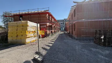 Neubauhäuser im Rohbauzustand an einem sonnigen Tag, umgeben von Bauzäunen und Materialien.