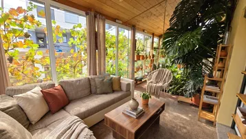 Helles Wohnzimmer im Wintergarten mit Holzdach, großen Fenstern und üppigen Pflanzen.