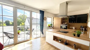 Moderne Küche mit Holzakzenten, Kochinsel und Zugang zu einem sonnigen Balkon mit Bergblick.