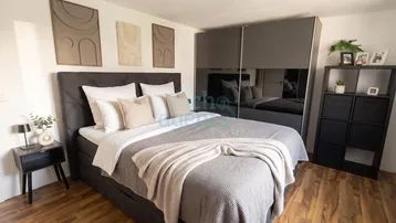 Modernes Schlafzimmer mit großem Bett, Spiegelschrank und Holzboden.