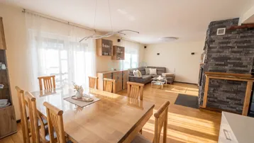 Geräumiger Wohn-Essbereich mit Holzboden, großem Esstisch und Kamin mit Steinverkleidung.