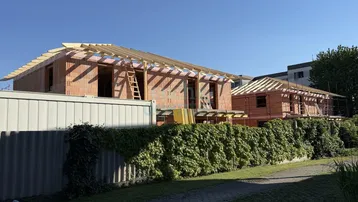 Neubau von Wohnhäusern im Rohbauzustand mit sichtbarer Dachkonstruktion an einem sonnigen Tag.