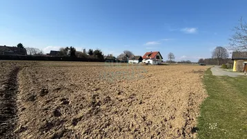 Großes Baugrundstück in ländlicher Umgebung mit Blick auf umliegende Häuser und weite Felder unter blauem Himmel.