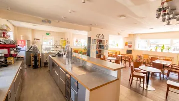 Geräumiger Innenbereich eines Cafés mit langer Theke, Vitrinen und mehreren Sitzbereichen.