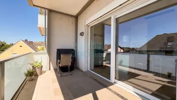 Geräumiger Balkon mit Fliesenboden und Blick auf die umliegende Wohngegend und Hügel.
