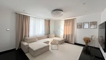 Helles Wohnzimmer mit großem Ecksofa, dunklem Fliesenboden und eleganter Deckenleuchte.