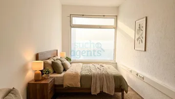Helles Schlafzimmer mit Holzbett, Nachttisch und großem Fenster, das viel Tageslicht hereinlässt.