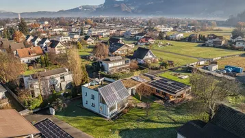 Weitläufige Wohnsiedlung mit Blick auf die umliegende Berglandschaft und grüne Felder unter blauem Himmel.